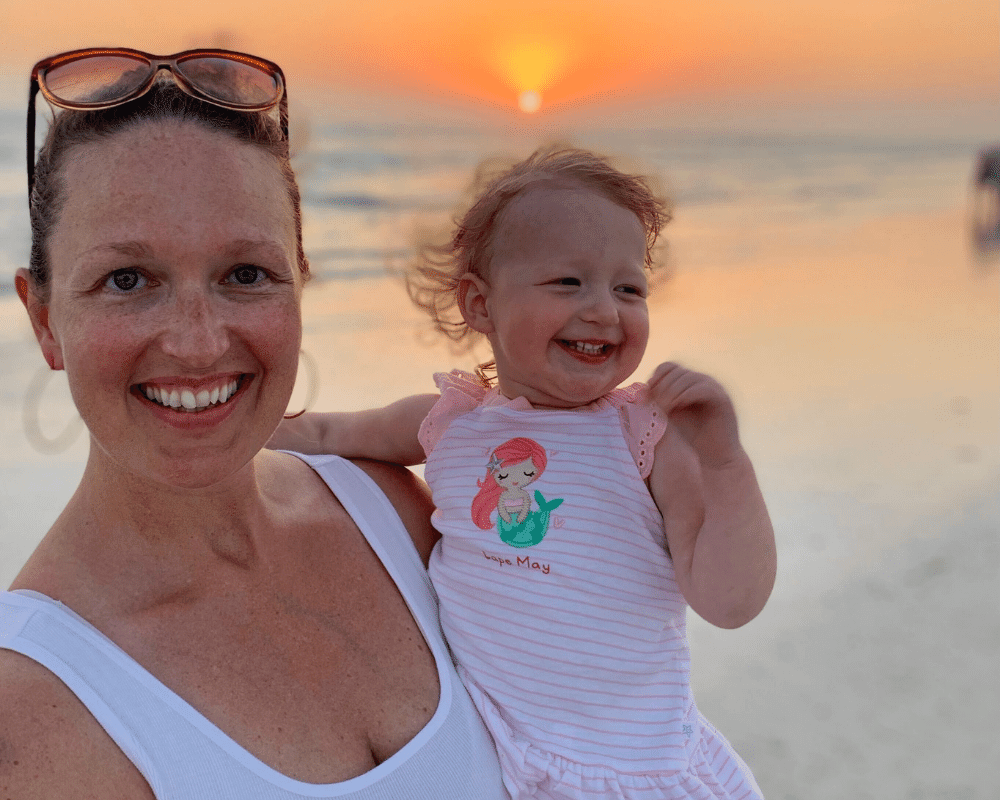 New mom Kristen holding her daughter in front of a sunset at the beach