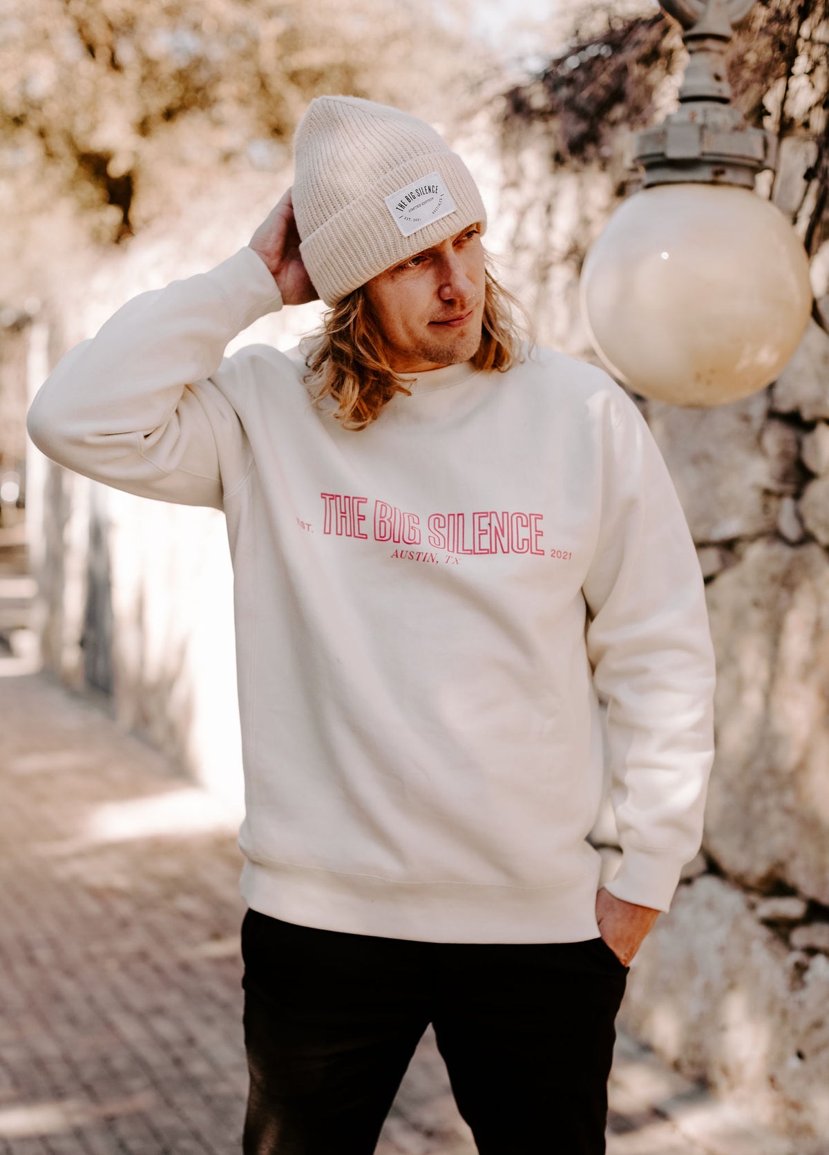 Bobby next to a stone wall in the bone TBS sweatshirt and beanie